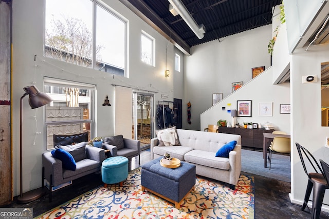 living room with concrete flooring, a tiled fireplace, and a towering ceiling