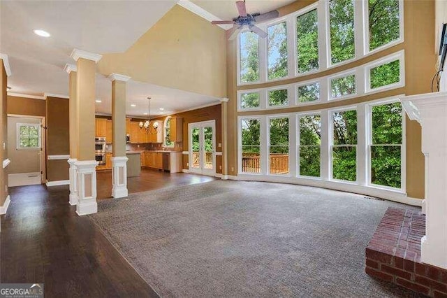 unfurnished living room with decorative columns, recessed lighting, a high ceiling, ornamental molding, and ceiling fan with notable chandelier