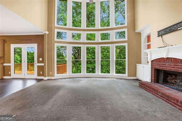 unfurnished living room featuring a towering ceiling, a brick fireplace, carpet, and baseboards