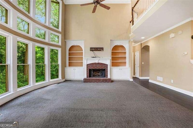 unfurnished living room featuring baseboards, arched walkways, crown molding, a brick fireplace, and built in shelves