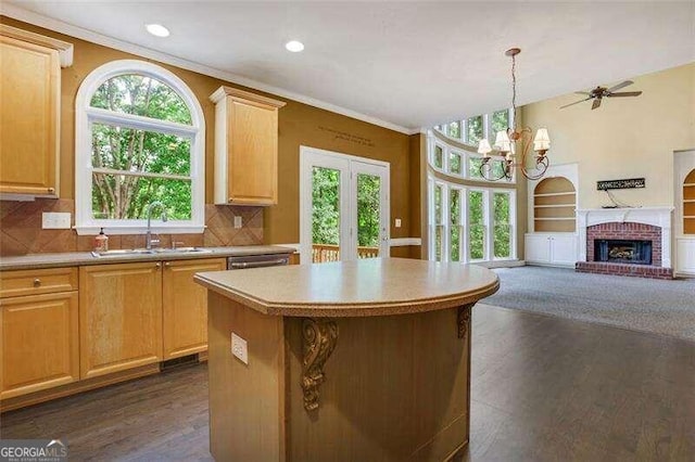 kitchen with ornamental molding, open floor plan, light countertops, a brick fireplace, and a sink