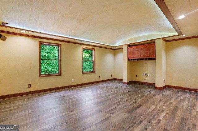 interior space with vaulted ceiling, crown molding, wood finished floors, and baseboards