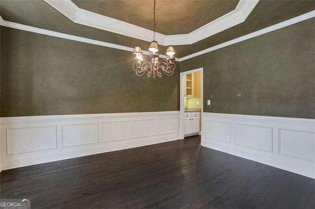 unfurnished dining area featuring dark wood-type flooring, wainscoting, an inviting chandelier, a raised ceiling, and crown molding