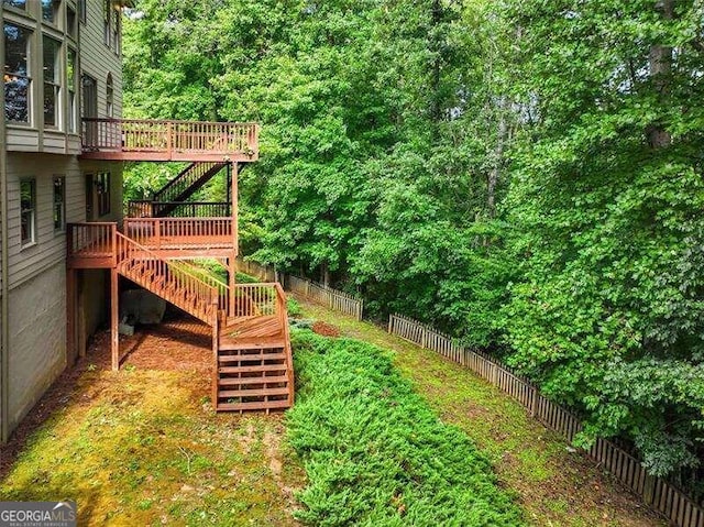 view of yard with fence, a wooden deck, and stairs