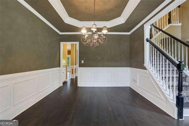 unfurnished dining area featuring dark wood-style floors, ornamental molding, an inviting chandelier, stairs, and a tray ceiling