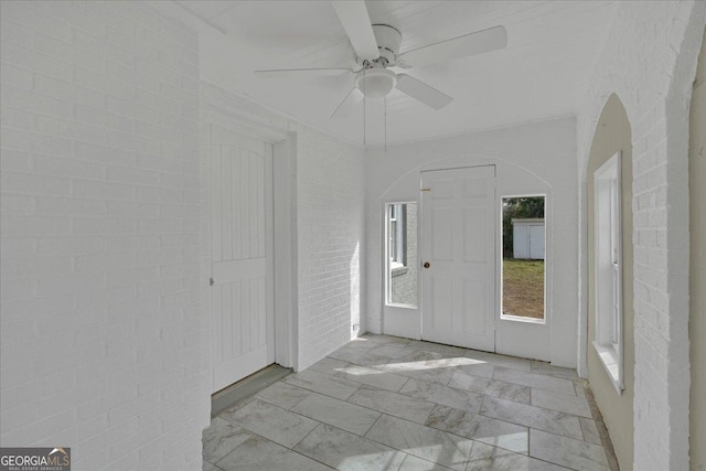 spare room with ceiling fan and brick wall