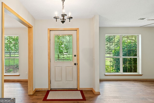 entryway with a textured ceiling, plenty of natural light, an inviting chandelier, and light hardwood / wood-style floors