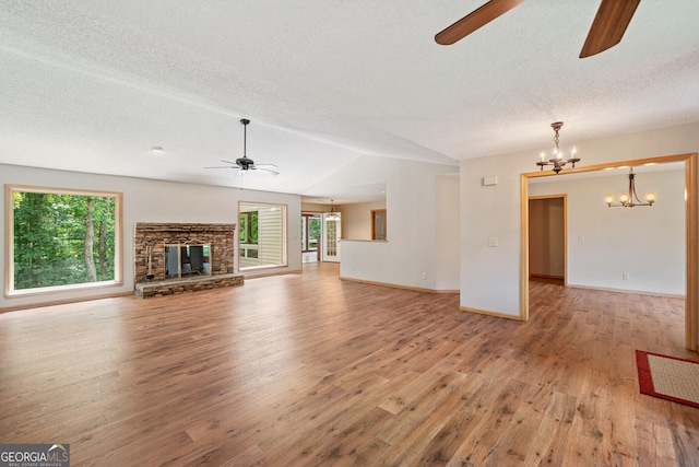 unfurnished living room with ceiling fan with notable chandelier, light hardwood / wood-style floors, lofted ceiling, a stone fireplace, and a textured ceiling