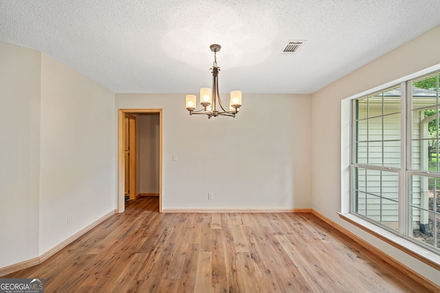 unfurnished dining area featuring a textured ceiling, light hardwood / wood-style flooring, and a chandelier