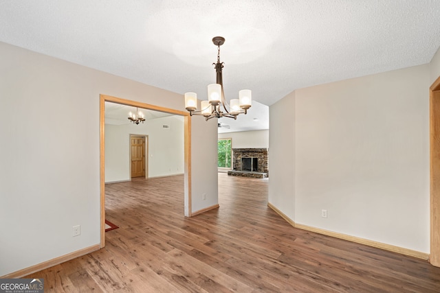 unfurnished dining area with a textured ceiling, a chandelier, wood-type flooring, and a stone fireplace