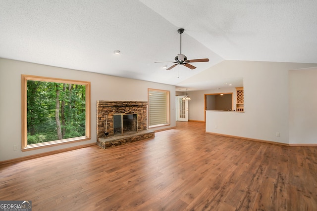 unfurnished living room featuring hardwood / wood-style floors, a textured ceiling, ceiling fan, a stone fireplace, and lofted ceiling