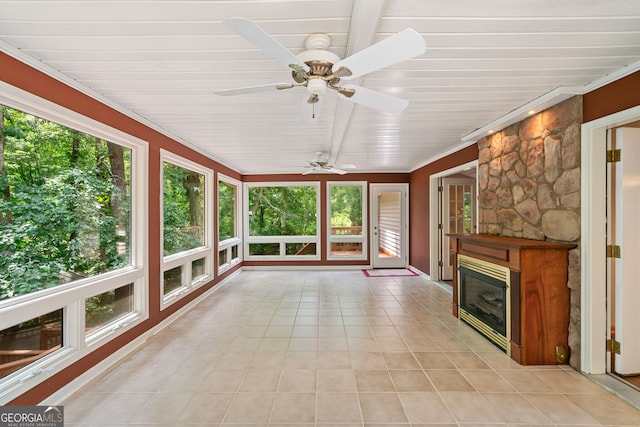 unfurnished sunroom featuring plenty of natural light, ceiling fan, and a stone fireplace