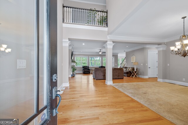 entrance foyer with decorative columns, ceiling fan with notable chandelier, light hardwood / wood-style flooring, and crown molding