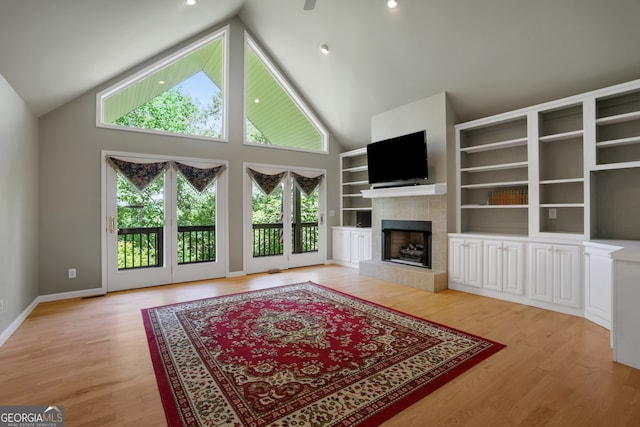 living room featuring plenty of natural light, high vaulted ceiling, a tiled fireplace, and light hardwood / wood-style floors