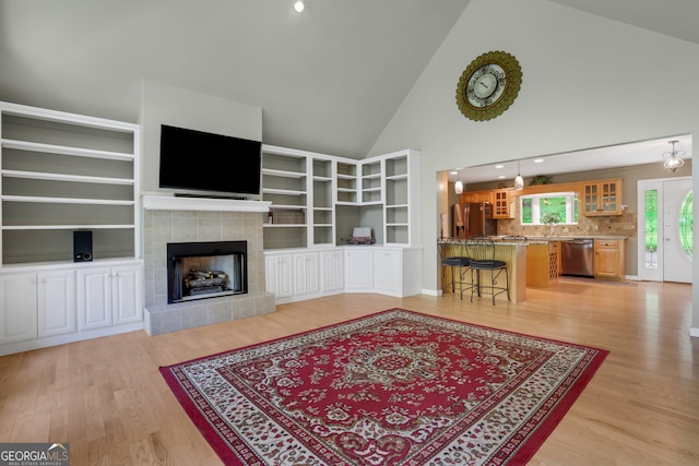 living room with high vaulted ceiling, a fireplace, and light wood-type flooring