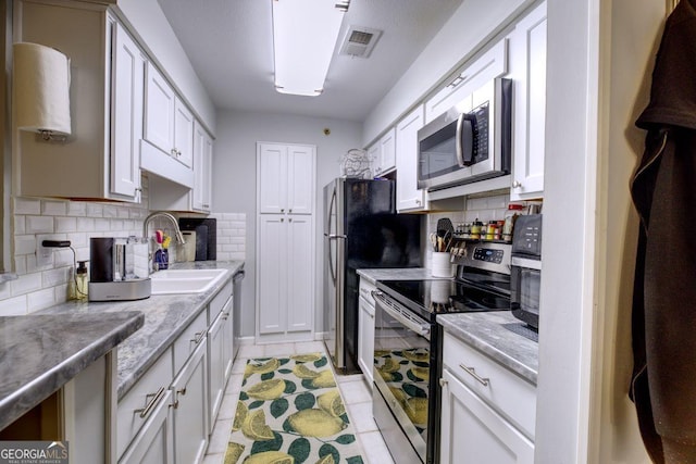 kitchen featuring sink, light tile patterned floors, tasteful backsplash, white cabinetry, and stainless steel appliances