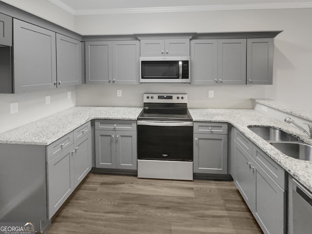 kitchen with sink, crown molding, appliances with stainless steel finishes, gray cabinetry, and light stone countertops