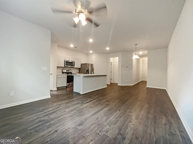 interior space featuring appliances with stainless steel finishes, hanging light fixtures, dark hardwood / wood-style floors, white cabinets, and a kitchen island