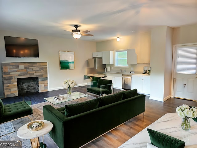 living room with dark wood-type flooring, ceiling fan, sink, and a stone fireplace