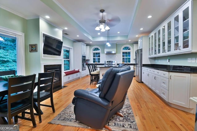 living room featuring sink, light hardwood / wood-style floors, ceiling fan, a raised ceiling, and crown molding