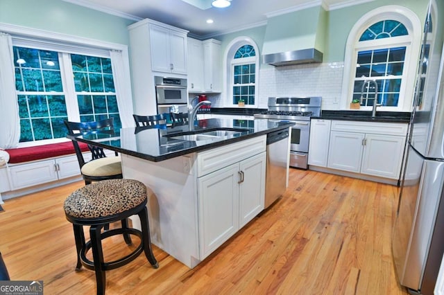 kitchen featuring appliances with stainless steel finishes, light hardwood / wood-style flooring, decorative backsplash, white cabinetry, and wall chimney range hood