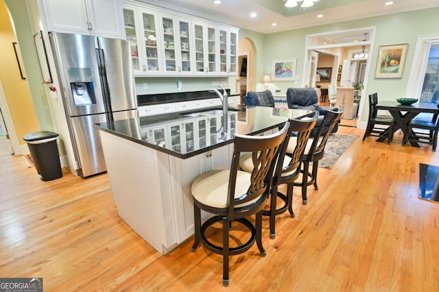 kitchen with stainless steel refrigerator with ice dispenser, sink, light wood-type flooring, white cabinets, and a kitchen breakfast bar