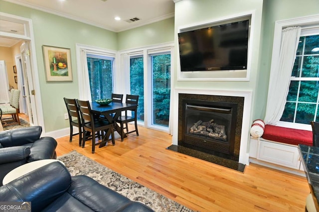 living room featuring a fireplace with flush hearth, visible vents, baseboards, light wood-style floors, and ornamental molding