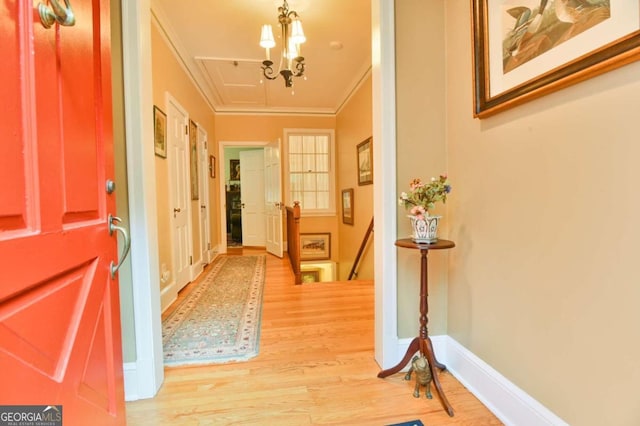 hall featuring a notable chandelier, ornamental molding, an upstairs landing, wood finished floors, and baseboards