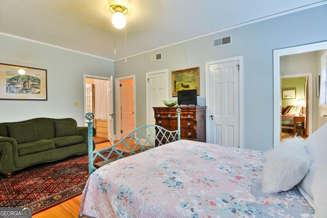 bedroom featuring wood finished floors, visible vents, and crown molding