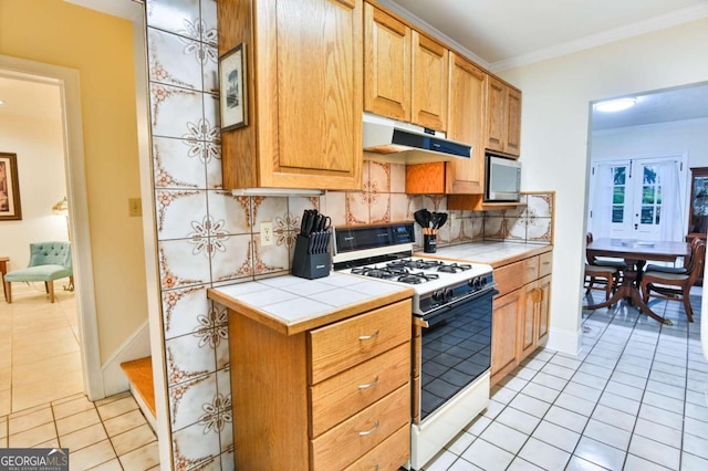 kitchen featuring backsplash, ornamental molding, tile counters, light tile patterned floors, and white range with gas cooktop