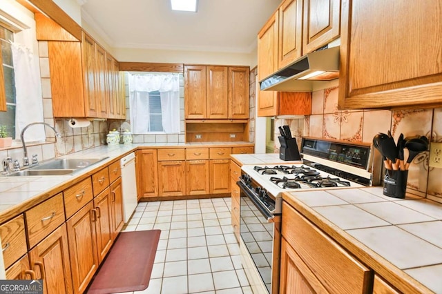 kitchen with tile countertops, a sink, under cabinet range hood, and gas range