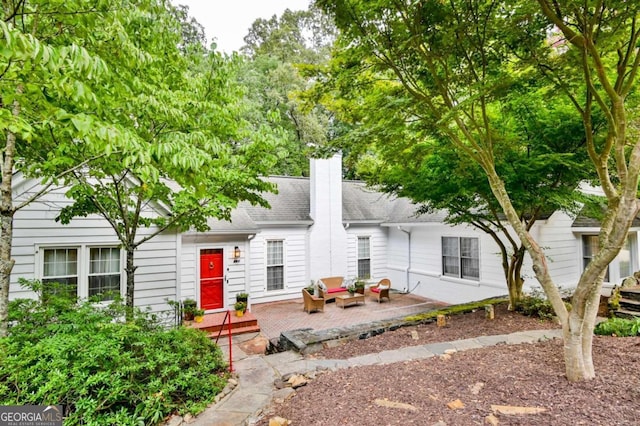 view of front of property featuring a patio area, a chimney, and roof with shingles