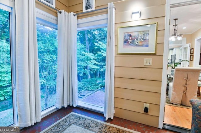 entryway featuring brick floor, ornamental molding, and a notable chandelier