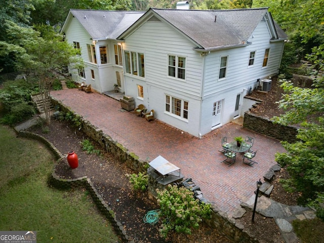 back of house featuring central air condition unit, a patio area, a chimney, and roof with shingles