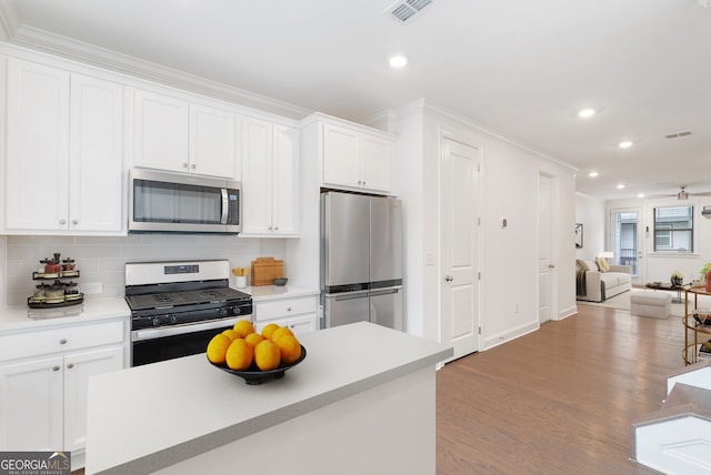 kitchen featuring white cabinetry, stainless steel appliances, ornamental molding, light hardwood / wood-style floors, and backsplash