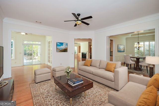 living room with crown molding, ceiling fan with notable chandelier, and light wood-type flooring