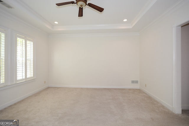 empty room featuring crown molding, a raised ceiling, light carpet, and ceiling fan