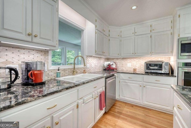 kitchen with light wood-type flooring, appliances with stainless steel finishes, decorative backsplash, sink, and white cabinets