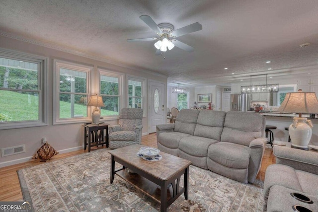 living room with ceiling fan, a textured ceiling, light wood-type flooring, and crown molding