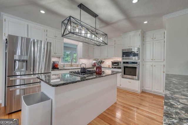 kitchen featuring stainless steel appliances, hanging light fixtures, a kitchen island, white cabinetry, and light hardwood / wood-style flooring