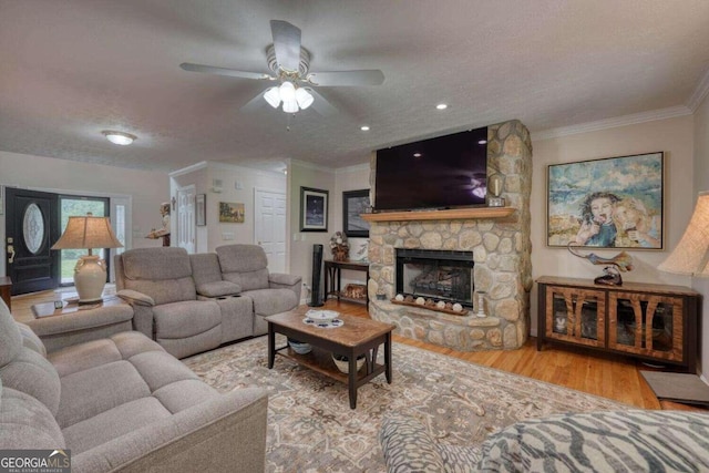 living room featuring a textured ceiling, ceiling fan, crown molding, a fireplace, and light hardwood / wood-style flooring