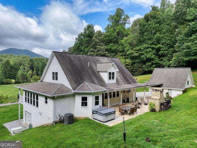 back of house featuring a hot tub, central air condition unit, a lawn, a patio area, and a mountain view