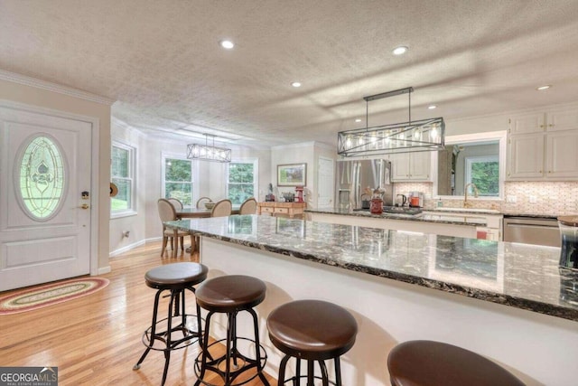 kitchen with hanging light fixtures, a textured ceiling, stainless steel appliances, and white cabinets