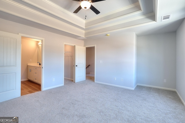 unfurnished bedroom featuring ceiling fan, a walk in closet, a tray ceiling, and crown molding