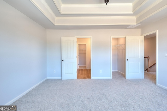 unfurnished bedroom with crown molding, carpet flooring, a tray ceiling, a walk in closet, and a closet