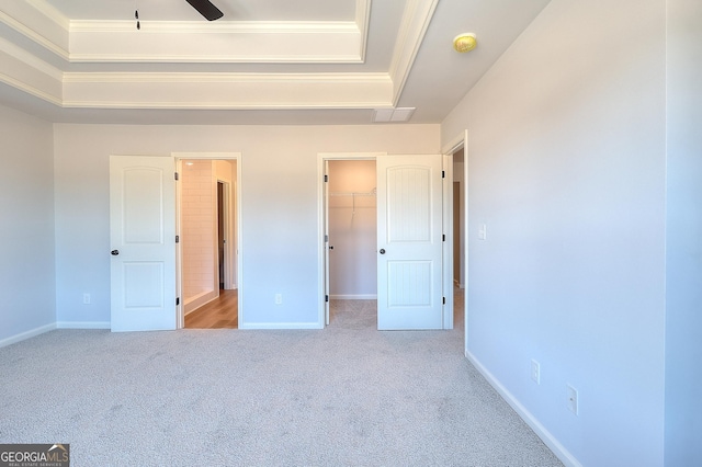 unfurnished bedroom with a walk in closet, a raised ceiling, a closet, and light carpet