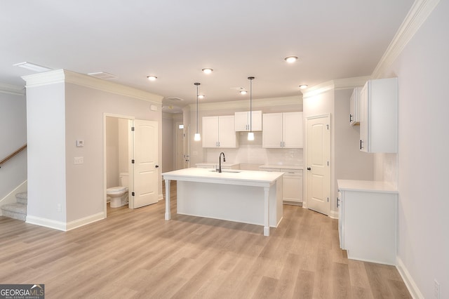 kitchen with tasteful backsplash, white cabinetry, an island with sink, hanging light fixtures, and ornamental molding