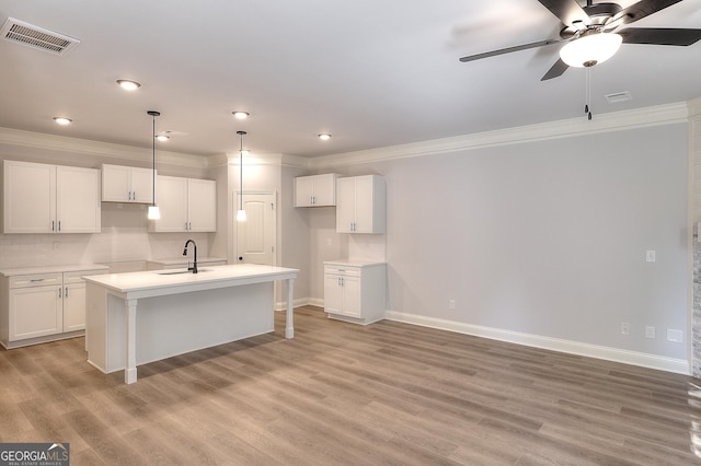 kitchen with pendant lighting, light hardwood / wood-style flooring, backsplash, white cabinets, and a center island with sink