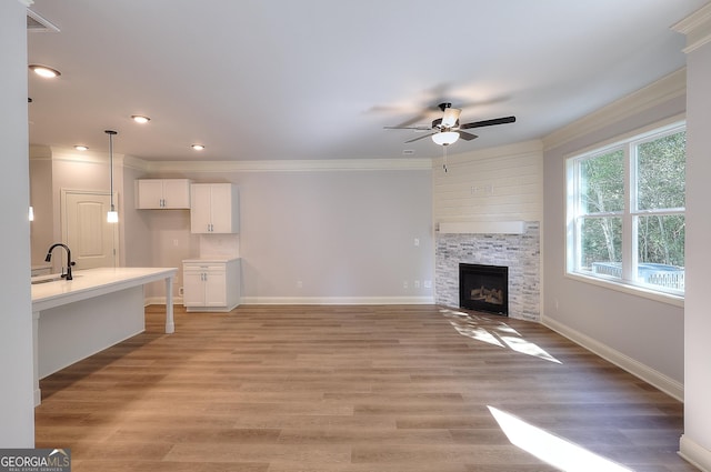 unfurnished living room featuring a fireplace, sink, ceiling fan, crown molding, and light hardwood / wood-style flooring