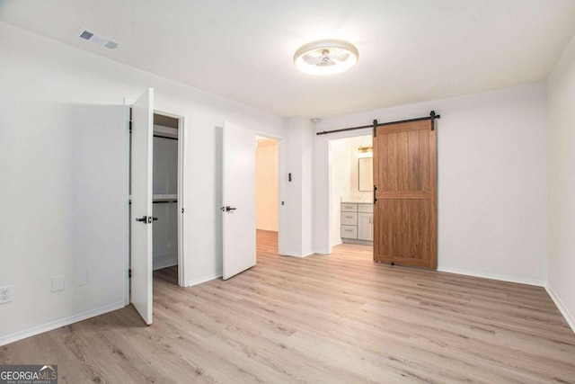 unfurnished bedroom featuring ensuite bathroom, a barn door, and wood-type flooring